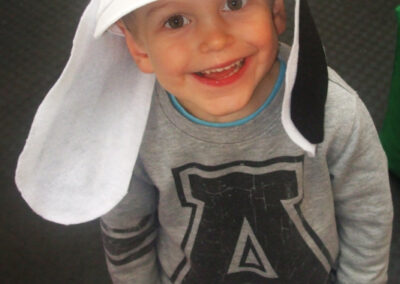 Boy smiles wearing a handmade dog cap, part of a "Cap Decorating" activity.