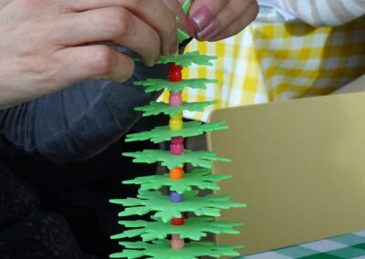 DIY Christmas tree craft: Hands assemble foam tree with beads on a wooden base.