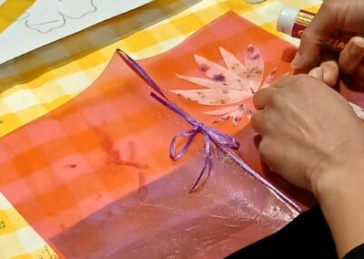 Crafters making floral art with paper, glue, and ribbon on a yellow checkered tablecloth.