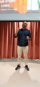 Man in dark blue shirt and tan pants speaking on stage